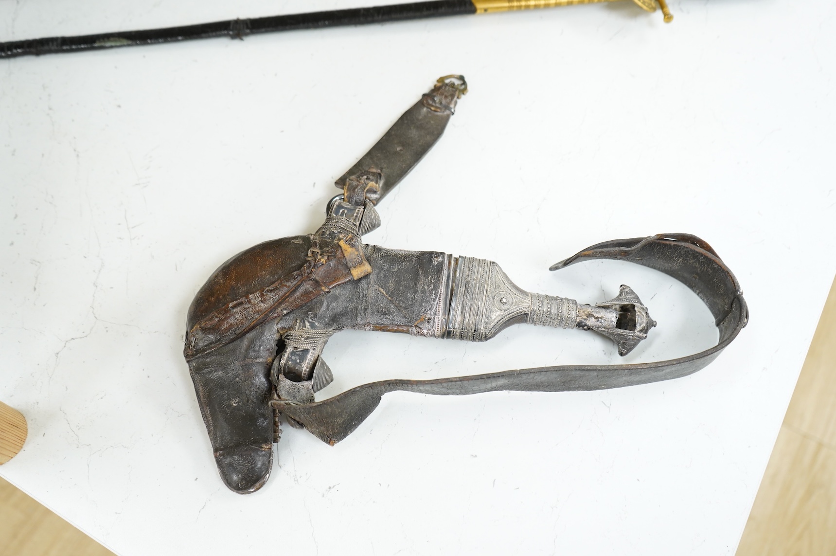 A late 19th century Arab silver mounted dagger jambya with silver filigree mounts to hilt and sheath, in its leather covered scabbard with parts of the original belt